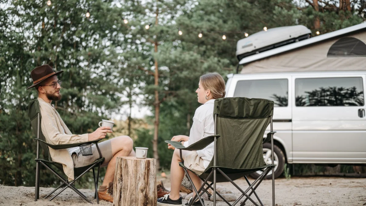Een stel geniet van een ontspannen moment met koffie tijdens een kampeervakantie in de natuur bij hun camper.