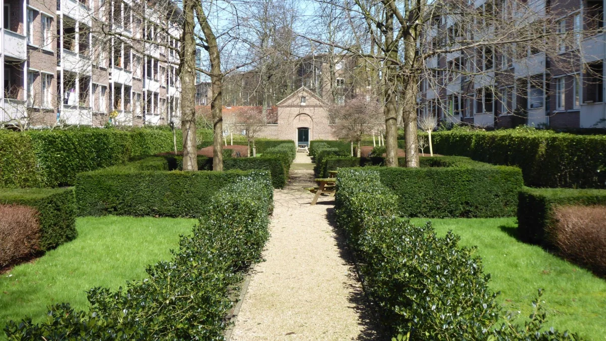 Prachtige groene binnenplaats in Amsterdam, met kleurrijke hagen, een pad en klassieke architectuur.