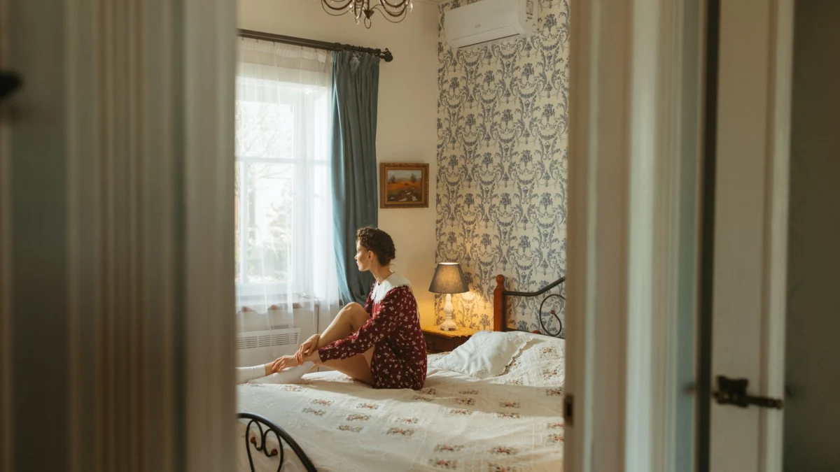 Volwassene zit op een bed in een zonnige slaapkamer, straalt warmte en rust uit.