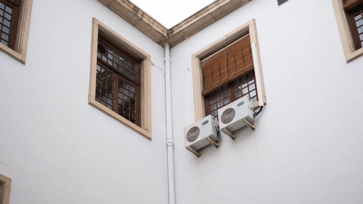 Witte gebouwgevel met houten raamshutters en airconditioningunits.