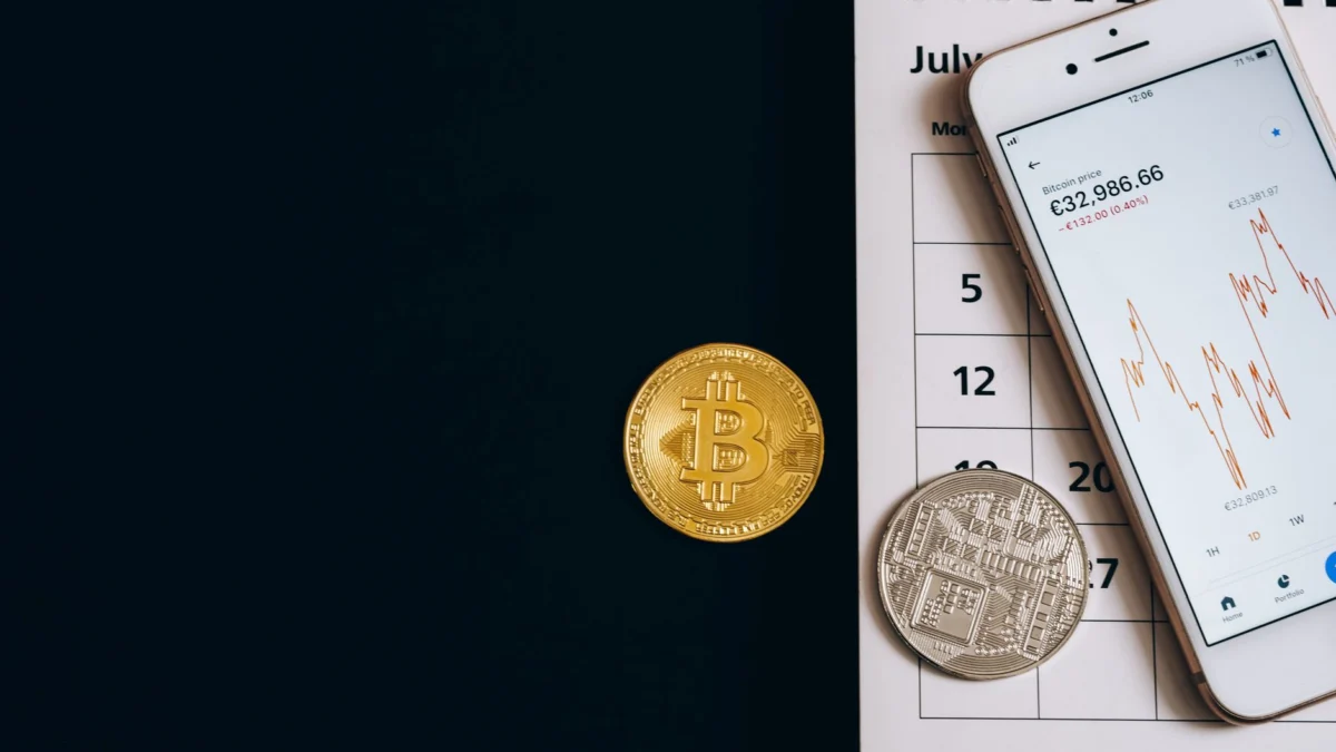 Bitcoin-munten op een kalender met een smartphone die prijs trends toont, ter illustratie van financiële dynamiek.