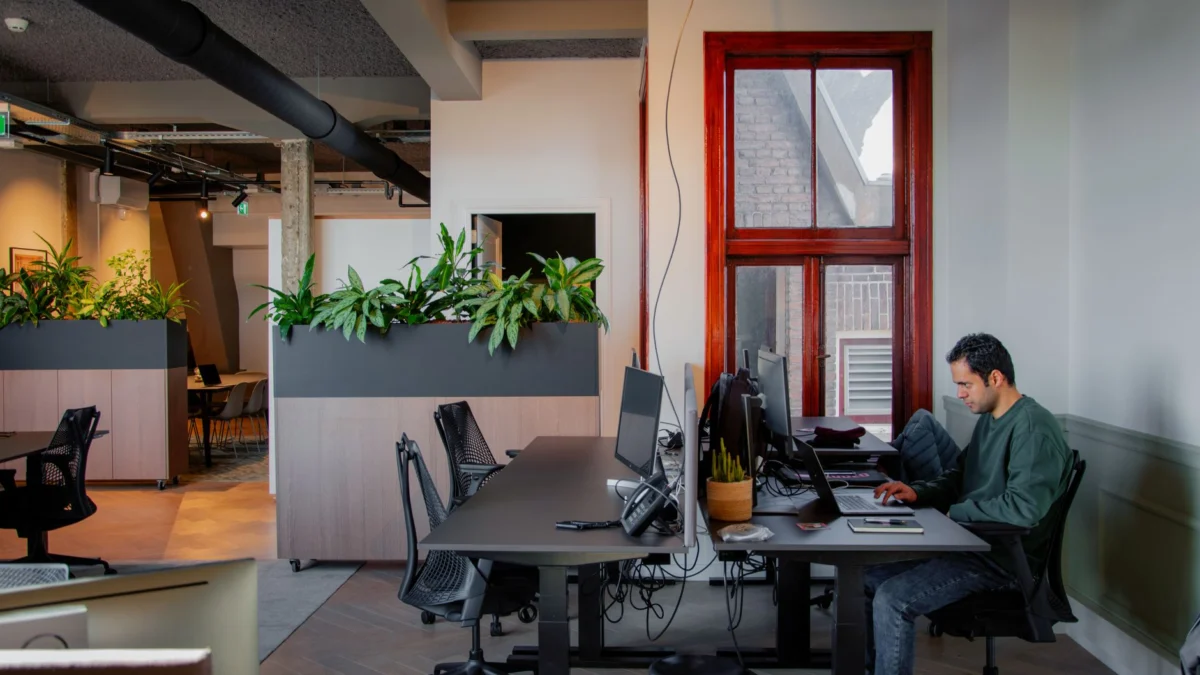 Professioneel werkend in een modern kantoor in Amsterdam met planten en natuurlijk licht, dat productiviteit en hedendaags design toont.