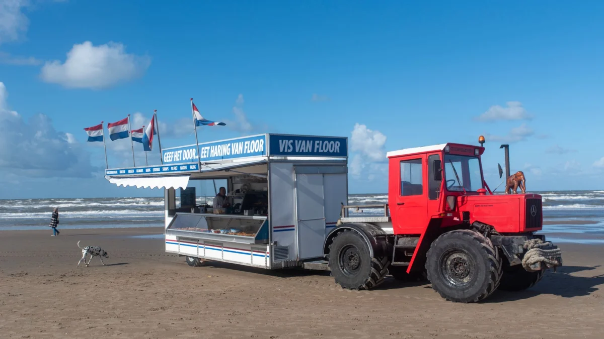 Een buitenvistrap met tractor op een Nederlands strand, met kleurrijke vlaggen die wapperen.