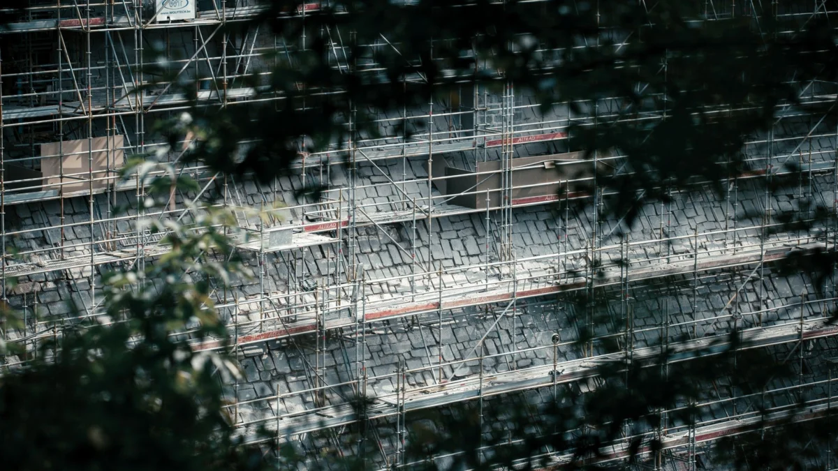 Hooghoekse kijk op scaffolding door bladeren, met een bouwproject in ontwikkeling in natuurlijk licht.