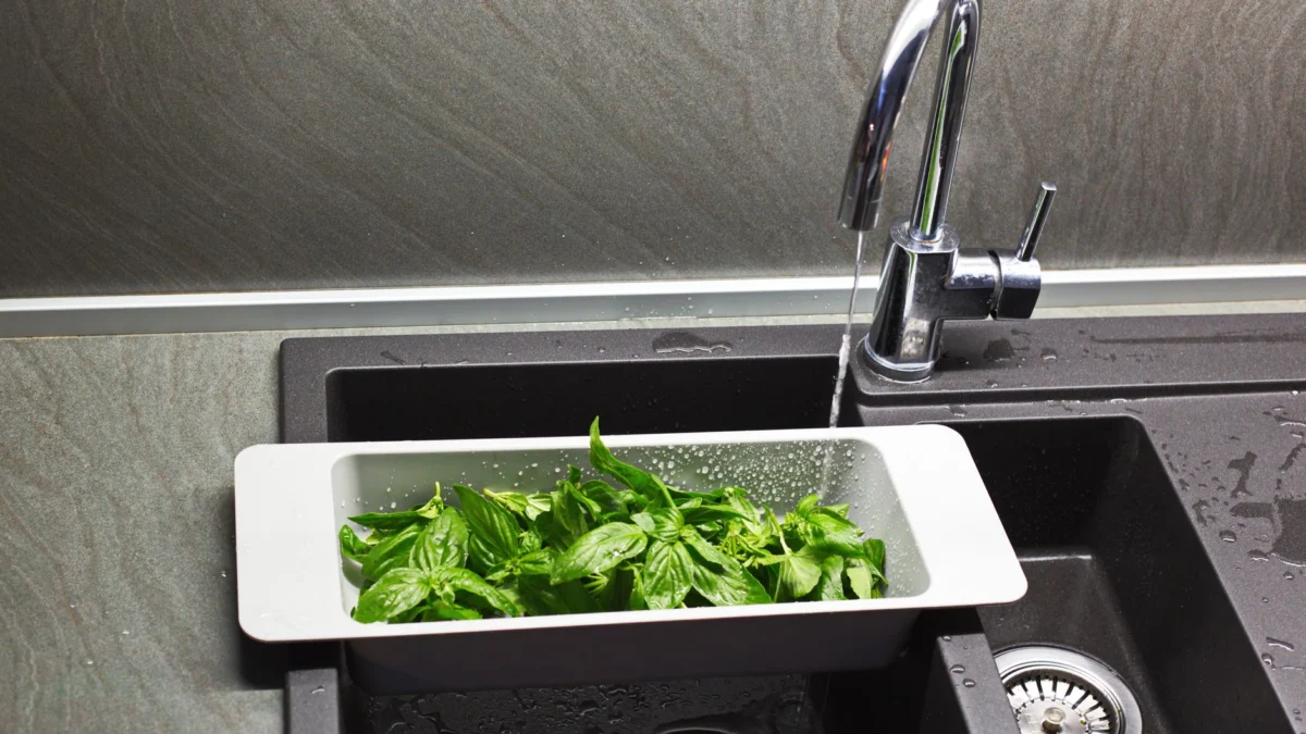 Verse basilicumblaadjes worden gewassen onder een stromende keukenkraan, ideaal voor culinaire toepassingen.