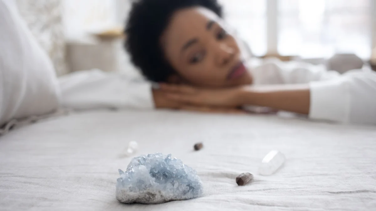 Een vrouw ontspant in een serene slaapkamer met helende kristallen op het bed, waardoor een gevoel van rust ontstaat.
