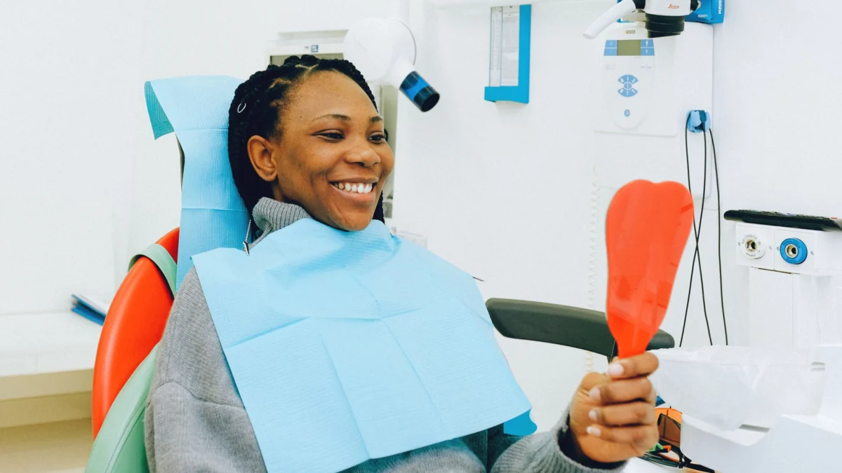 Glunderende vrouw die een spiegel vasthoudt tijdens een tandheelkundig onderzoek in een kliniek.