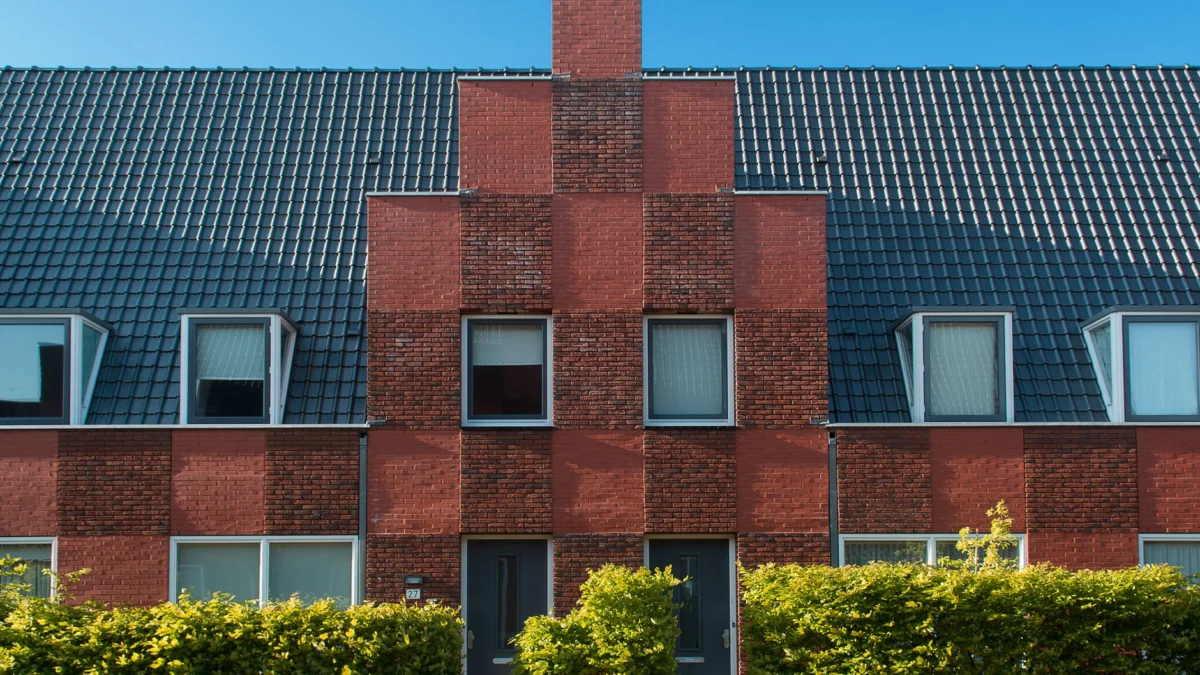 Contemporary bakstenen stadswoning gevel met nette haag onder een heldere blauwe lucht.