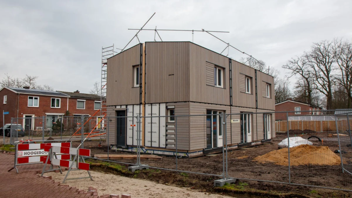 Een modern huis in aanbouw met steigers, hekken en bouwborden op een bewolkte dag.