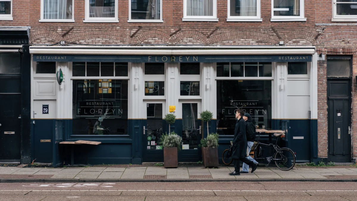 Straatbeeld van voetgangers die langs een charmant restaurant in Amsterdam lopen.