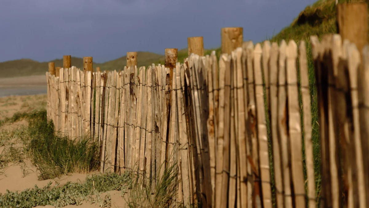 Een houten schutting langs de kust, op zandduinen in Ierland, onder een dreigende hemel.