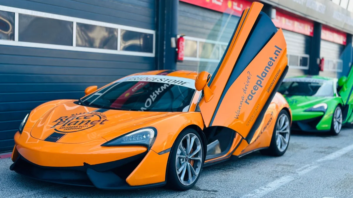 Een gestroomlijnde oranje sportwagen met open deuren geparkeerd op het racecircuit. Klaar voor actie!