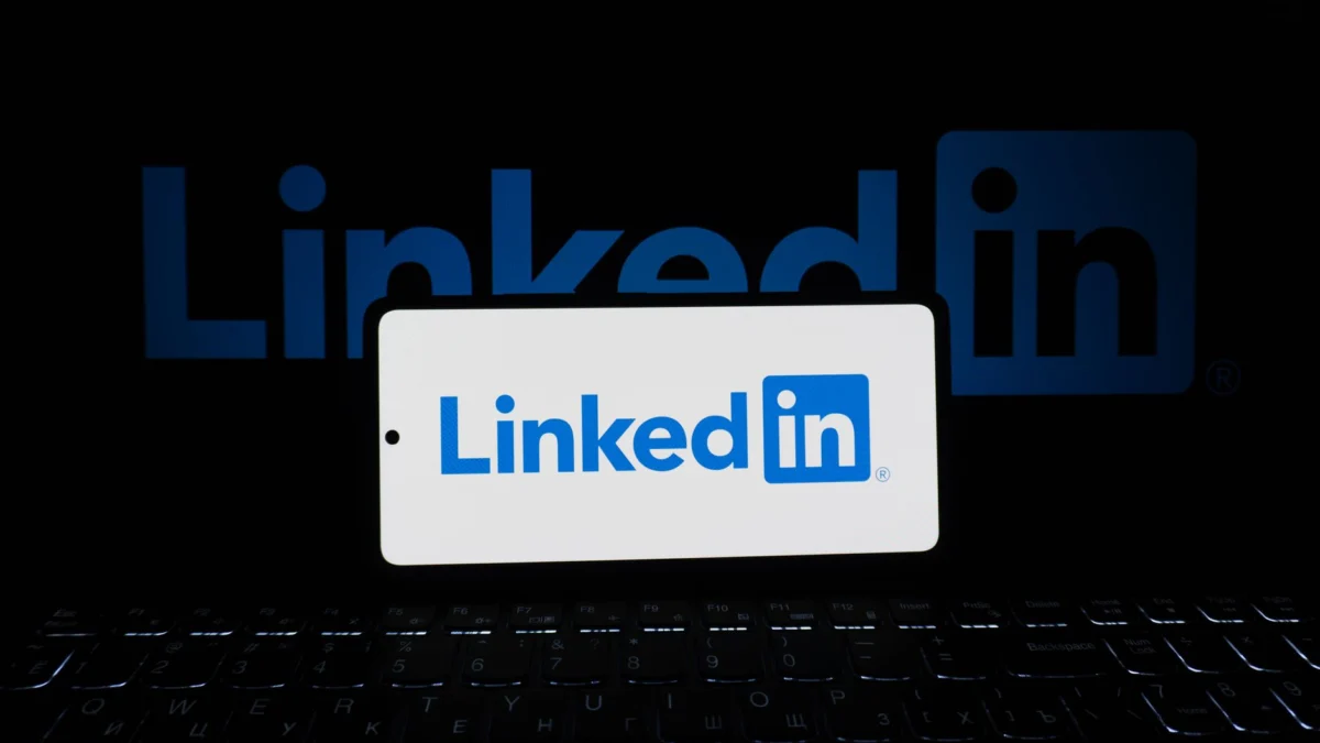 Smartphone met LinkedIn-logo, toetsenbord en groot logo op de achtergrond, zakelijk thema.