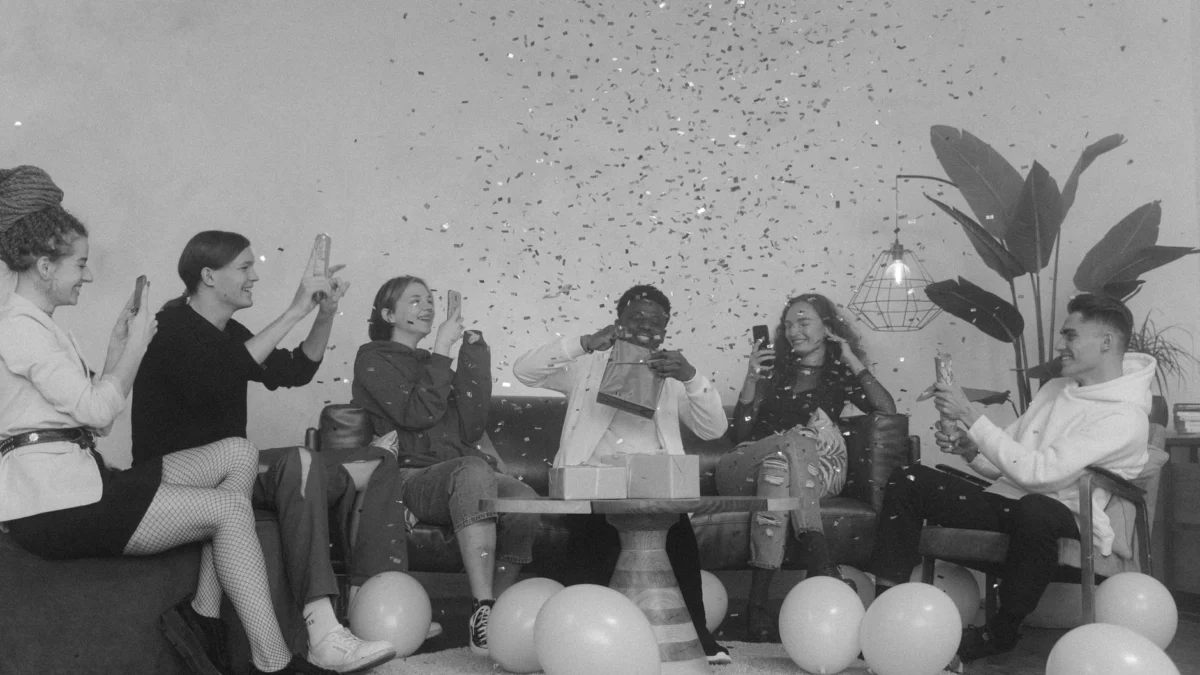 Een levendige zwart-wit bijeenkomst van vrienden die binnen vieren met ballonnen en confetti.