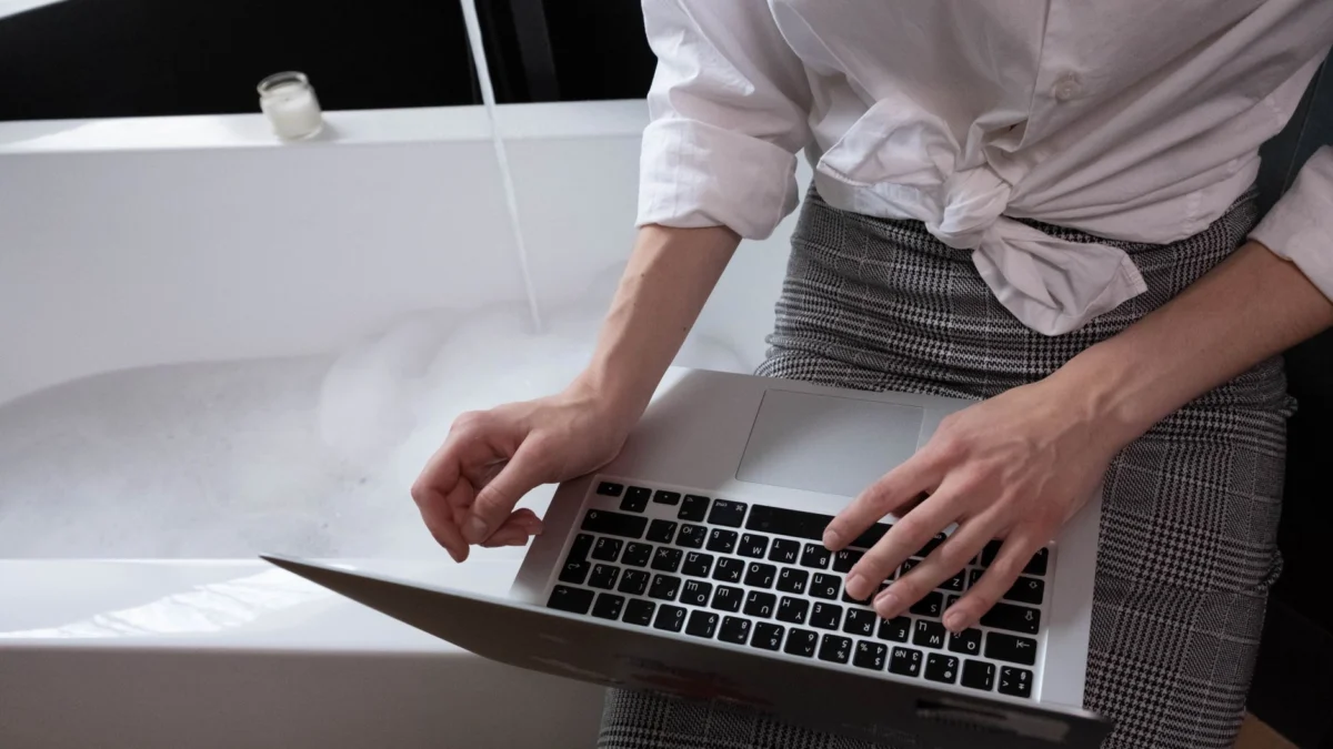 Volwassen vrouw werkt op een laptop terwijl ze naast een met bubbels gevuld bad zit, werk en ontspanning combineren.
