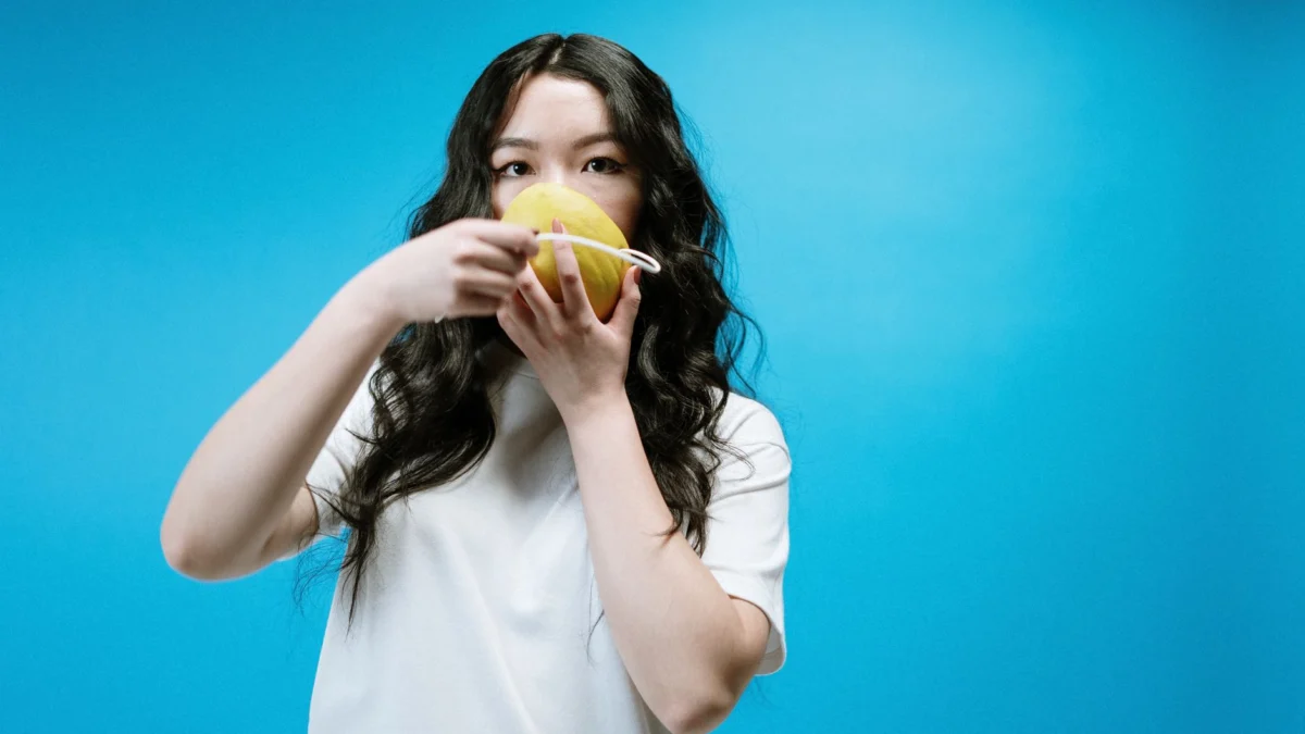 Jonge vrouw gebruikt op humoristische wijze een fruit als DIY-masker tijdens de quarantaine.