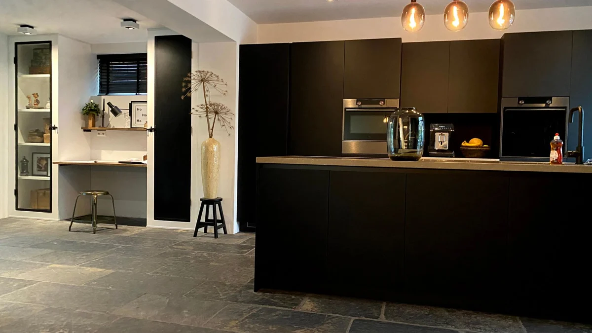 Moderne keuken met zwarte kasten, stenen vloeren en minimalistische decoraties geaccentueerd door hanglampen.