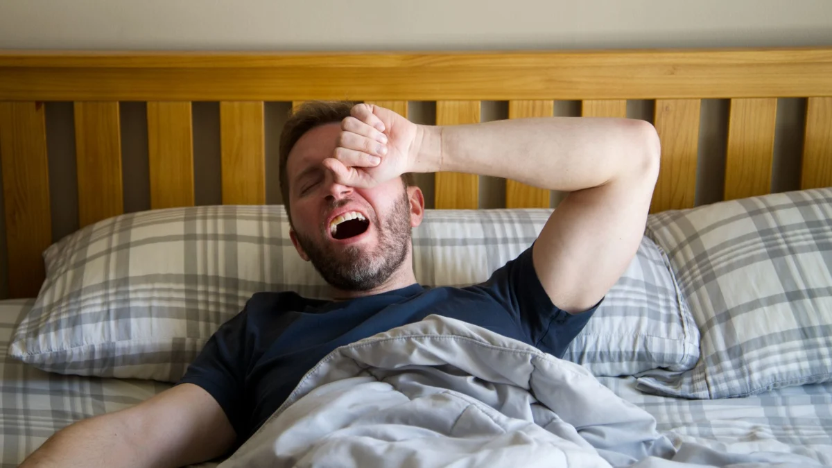 Man die gaapt en wakker wordt in bed, begint een nieuwe dag met het ochtendlicht.