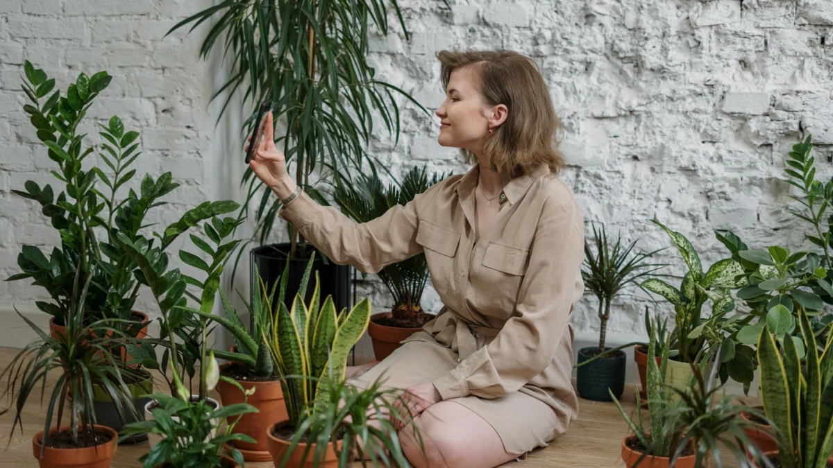 Een vrouw maakt een selfie terwijl ze omringd is door verschillende kamerplanten binnen.