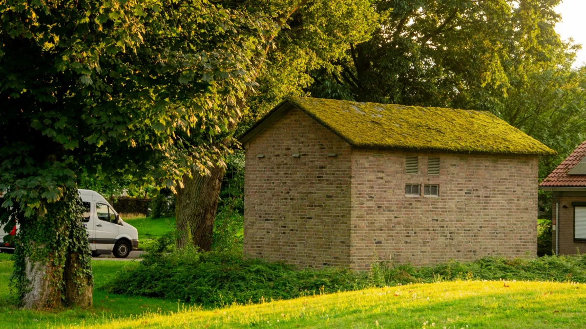 Een charmante rustieke stenen schuur met een met mos bedekt dak, genesteld in een levendige zomertuin.