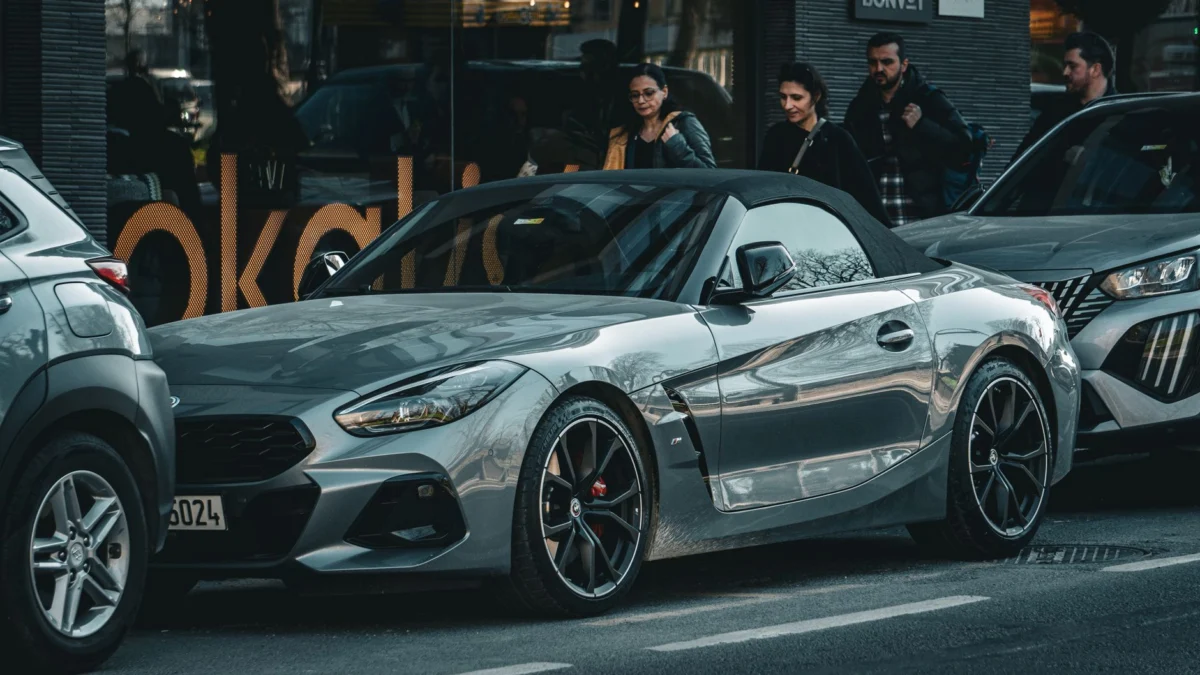Grijze BMW Z4 roadster geparkeerd op een drukke stadsstraat met voorbijgangers, die de stedelijke levensstijl vastlegt.