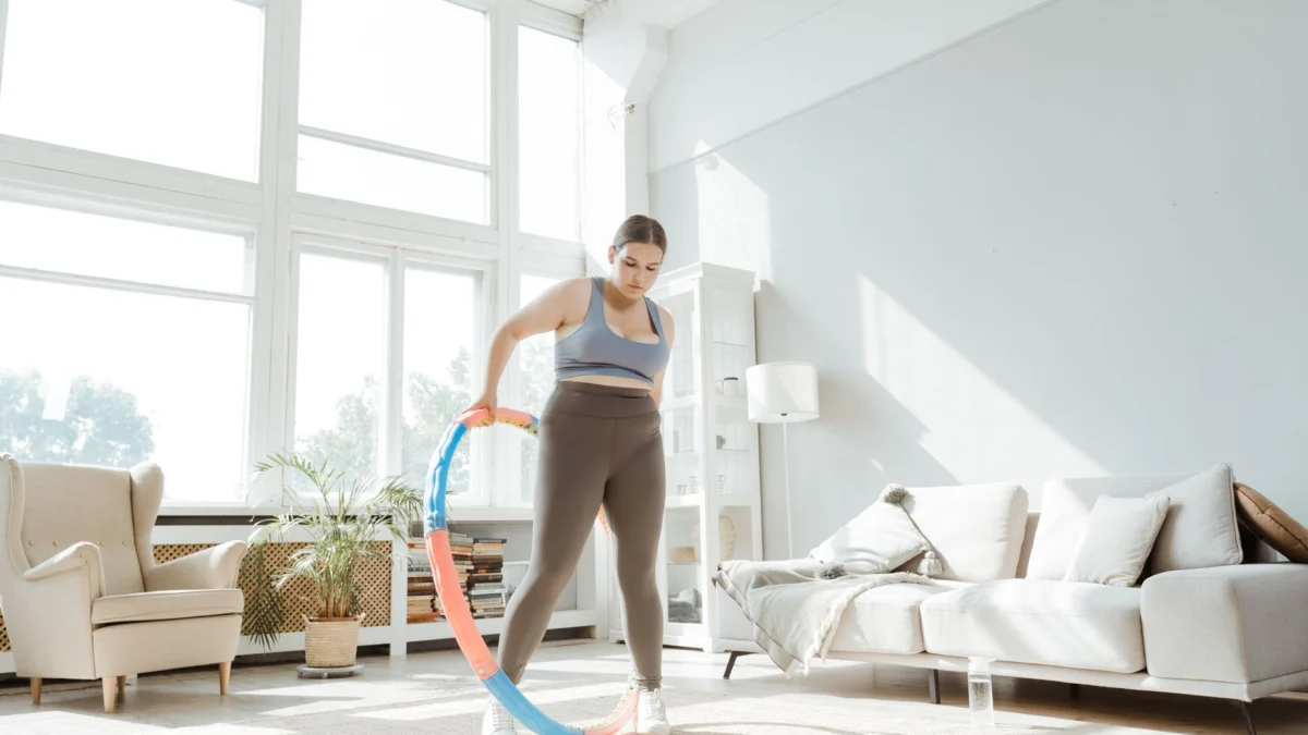 Een vrouw doet een hula hoop workout in een heldere, moderne woonkamer, wat welzijn en gezond leven bevordert.