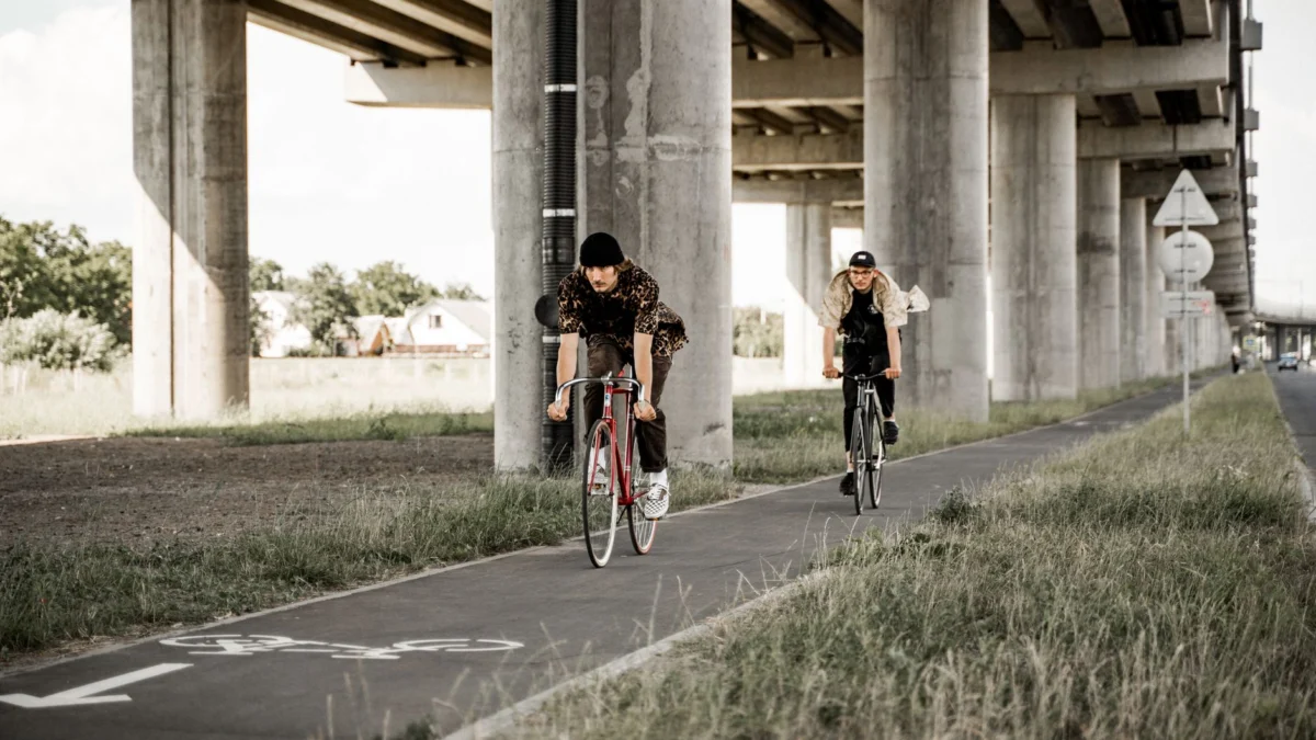 Twee jonge mannen genieten van een casual fietstocht op een aangewezen fietsstrook onder een stedelijke brug.