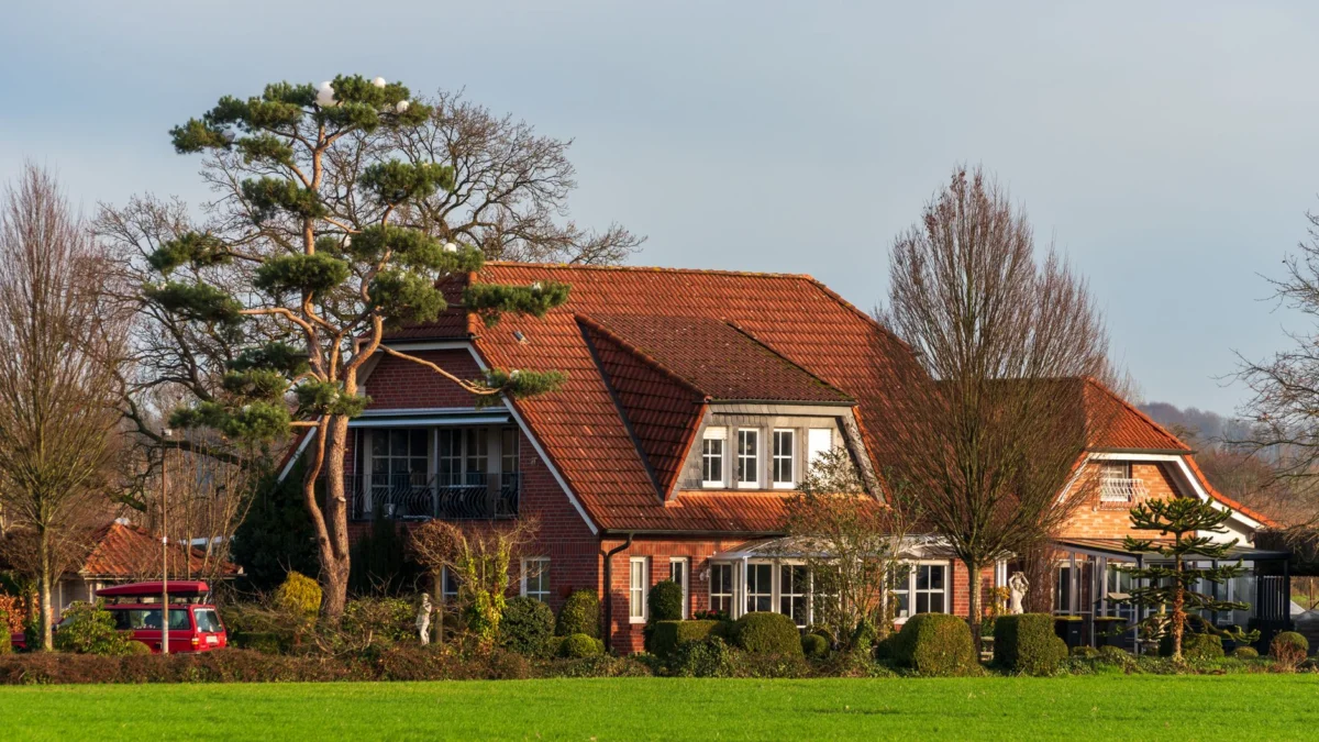 Een pittoreske landelijke woning met een rood dak te midden van een weelderig groen landschap en bomen, vastgelegd op een zonnige dag.