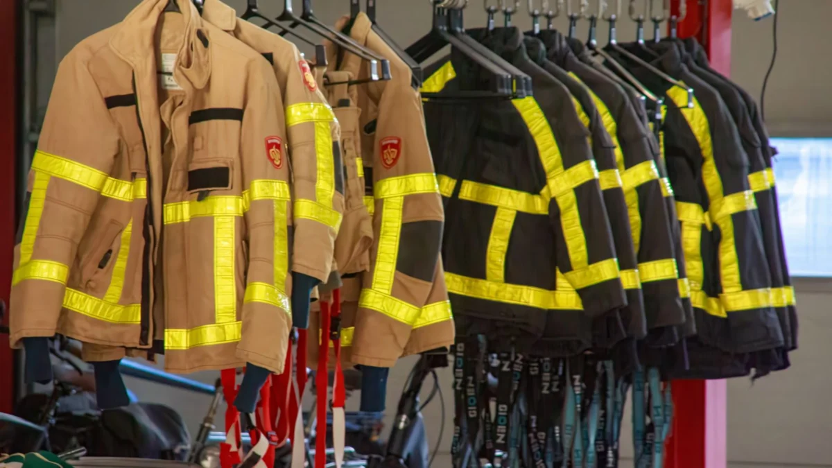 Brandweeruniformen met reflecterende strepen hangen in een garage.