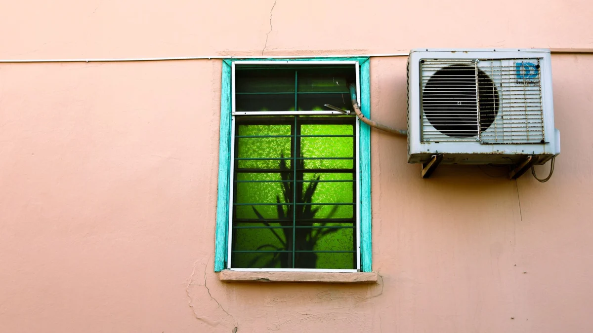 Foto van een muur met een raam waarin groene reflecties te zien zijn, naast een airconditioningunit.